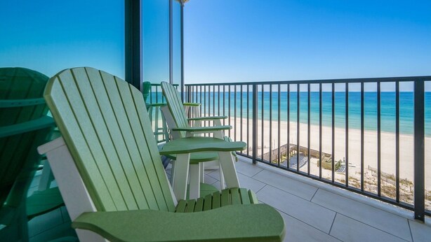 Un balcon avec des fauteuils Adirondack verts donnant sur une plage.