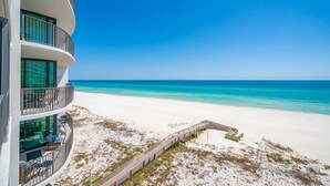 Un hôtel situé en bord de mer, doté d’un balcon incurvé, d’une plage de sable et surplombant un ciel bleu azur.