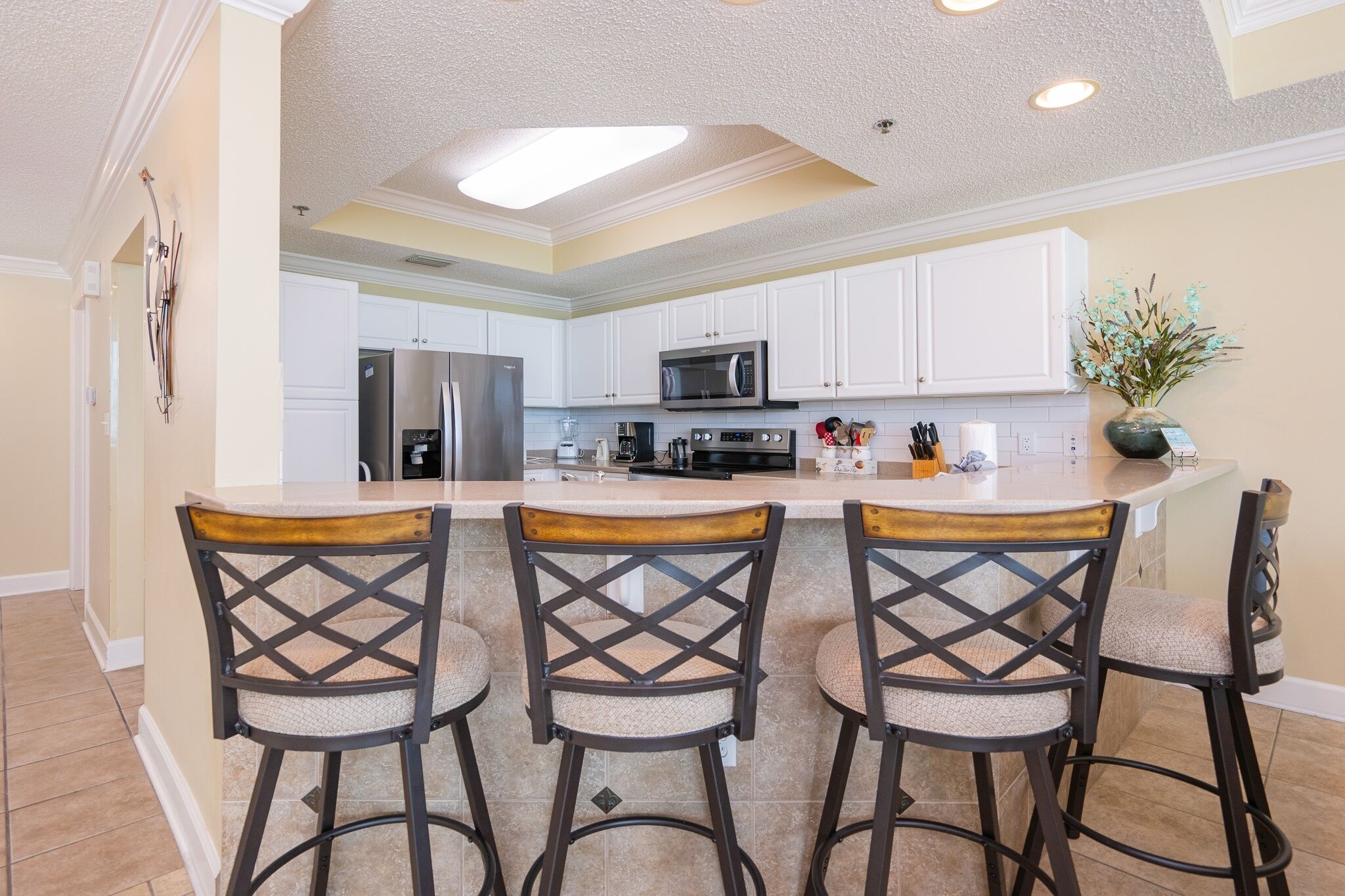A kitchen with white cabinets, a stainless steel refrigerator, a microwave, and a large island with bar stools.