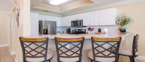 A kitchen with white cabinets, a stainless steel refrigerator, a microwave, and a large island with bar stools.