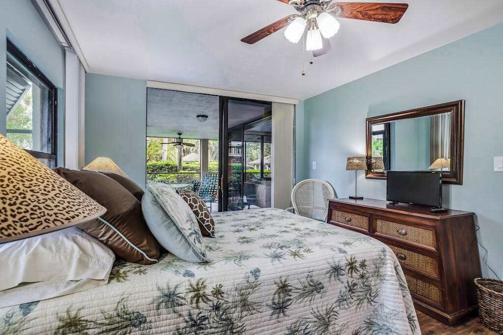 Une chambre à coucher comprenant un lit, un ventilateur de plafond, une commode, un téléviseur et une grande fenêtre.