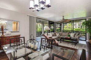A spacious living area with a glass dining table, a sofa, and a ceiling fan. - Spacious, air-conditioned condo with private W/D, beach shuttle, & central AC (Bonita Springs)