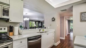 Een moderne keuken met witte kasten, een inbouwoven, een vaatwasser en een groot raam dat zorgt voor natuurlijk licht.