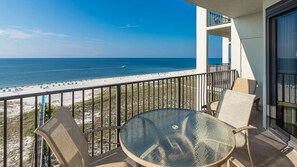 Ein Balkon mit Glastisch und Stühlen, der auf einen Strand mit freiem Blick auf das Meer und ein weit entferntes Boot blickt.