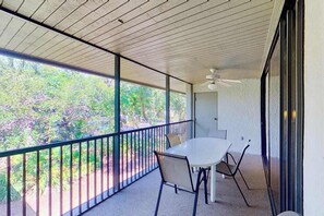 Ein Balkon mit Tisch und Stühlen, einem Deckenventilator und Blick auf Bäume.