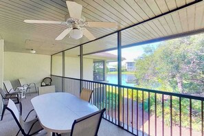 Ein Balkon mit Tisch und Stühlen, einem Deckenventilator und Blick auf Grünflächen und Gebäude.