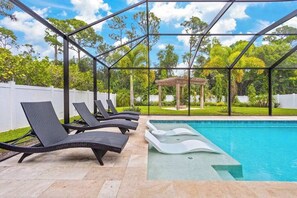 Ein Poolbereich mit Liegestühlen, einer Pergola und Blick auf Bäume.