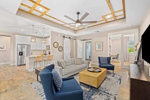 Ein geräumiger Wohnbereich mit Deckenventilator, einer Couch, einem Couchtisch und einer Küche im Hintergrund.