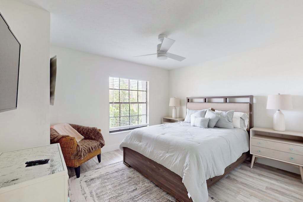 A bedroom with a bed, nightstands, a chair, a ceiling fan, and a window.