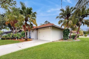Ein Bungalow mit Garage, umgeben von Palmen und einem gepflegten Rasen.