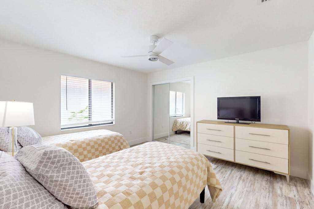 A bedroom with two beds, a TV, a ceiling fan, and a dresser.