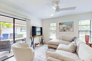 Ein Wohnzimmer mit Sofa, Sessel, Fernseher, Deckenventilator und Kunstwerk an der Wand.