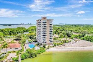 A high-rise hotel with a pool, surrounded by lush greenery and a beach. - Panoramic water views, pool, private beach, AC, WIFI and close to Gulf beaches (Bonita Springs)
