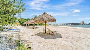 A beach with thatched umbrellas, lounge chairs, and a pier in the background. - Panoramic water views, pool, private beach, AC, WIFI and close to Gulf beaches (Bonita Springs)