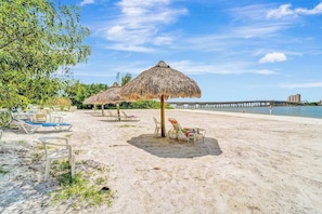 A beach with thatched umbrellas, lounge chairs, and a pier in the background. - Panoramic water views, pool, private beach, AC, WIFI and close to Gulf beaches (Bonita Springs)