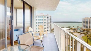 A balcony with a view of the ocean and buildings, a table, and two chairs. - Panoramic water views, pool, private beach, AC, WIFI and close to Gulf beaches (Bonita Springs)