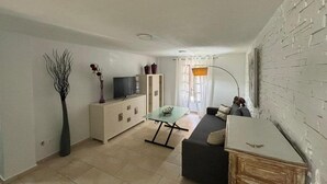 En moderne stue med sofa, sofabord, fjernsyn på et skab, en vase med planter og en murstensvæg.