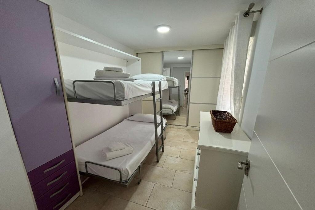 A dormitory room with bunk beds, a small cabinet, and a window with curtains.