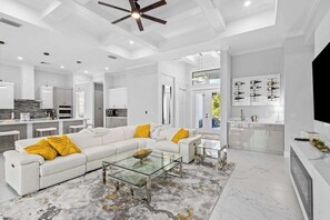 A modern living room with a white sectional sofa, glass coffee table, and a ceiling fan. - Luxe brand-new home with designer interior, lanai, private pool, & spa (Bonita Springs)