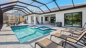 Ein Swimmingpool mit Liegestühlen, einer überdachten Terrasse und einem verglasten Bereich.