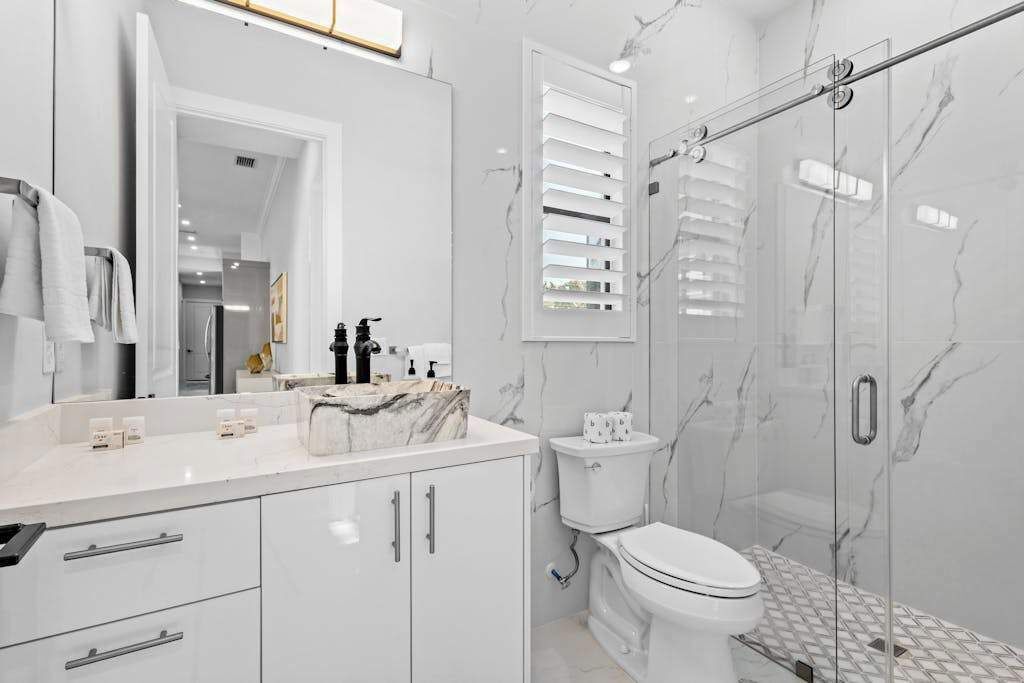 Ein modernes Badezimmer mit Marmorwaschbecken, Toilette und Duschkabine aus Glas.