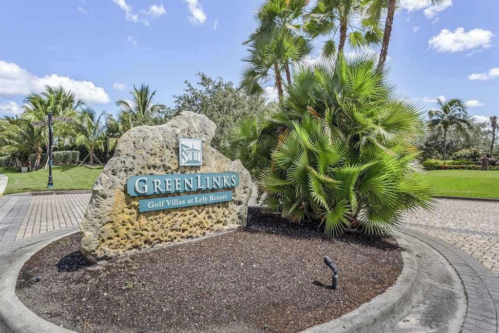 A sign for Green Links Golf Villas at Lely Resort, surrounded by palm trees and a paved walkway.