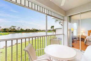 A balcony with a view of a lake, a table, and chairs. - Spacious 2nd-floor condo with lake/golf view - walk to restaurant, tennis & pool (Naples)