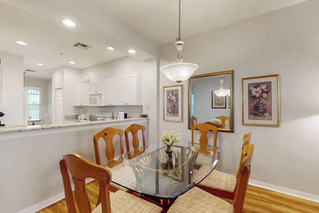 A dining area with a glass table surrounded by wooden chairs, a hanging light fixture, and framed artwork on the wall.