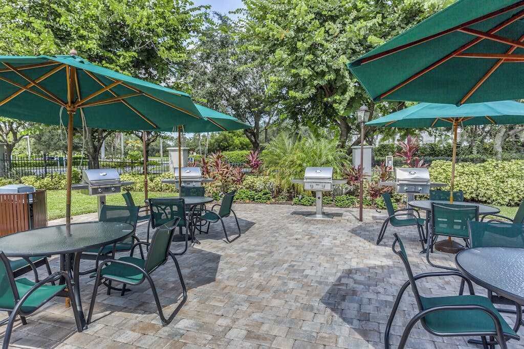 An outdoor patio with green umbrellas, metal chairs, and barbecue grills.