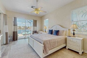 Ein Schlafzimmer mit Bett, Nachttischen, Deckenventilator und Blick ins Freie.