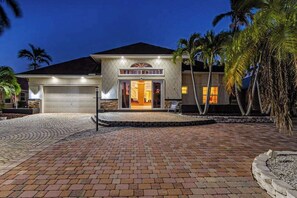 A two-story house with a garage, a driveway, and palm trees. - Striking European-style home w/ private pool, hot tub & river access via dock (Cape Coral)