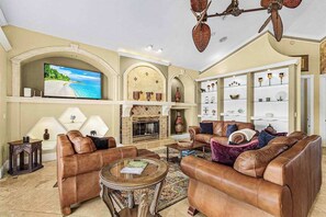 A living room with leather sofas, a fireplace, a television, and decorative shelves. - Striking European-style home w/ private pool, hot tub & river access via dock (Cape Coral)