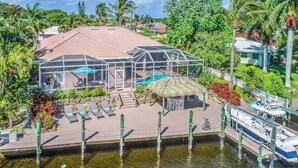 Una casa con piscina, terraza techada y muelle con barcos.