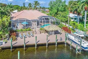 A house with a pool, covered patio, and dock with boats. - Custom waterfront home w/ dock, heated pool, AC & amazing indoor/outdoor spaces (Cape Coral)