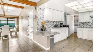 A modern kitchen with white cabinets, a marble countertop, and a tiled backsplash. - Spacious waterfront home with private pool & grill - near downtown (Cape Coral)