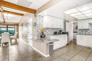 A modern kitchen with white cabinets, a marble countertop, and a tiled backsplash. - Spacious waterfront home with private pool & grill - near downtown (Cape Coral)