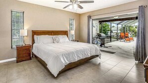 A bedroom with a bed, nightstand, ceiling fan, and a view of the outside. - Spacious waterfront home with private pool & grill - near downtown (Cape Coral)