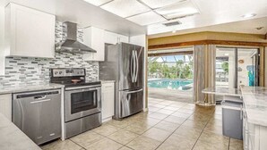A modern kitchen with stainless steel appliances, a tiled backsplash, and a view of a swimming pool. - Spacious waterfront home with private pool & grill - near downtown (Cape Coral)