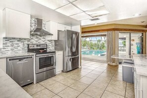 A modern kitchen with stainless steel appliances, a tiled backsplash, and a view of a swimming pool. - Spacious waterfront home with private pool & grill - near downtown (Cape Coral)