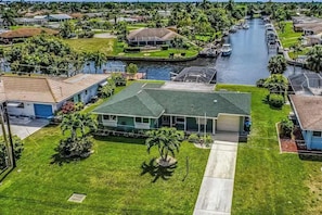 A residential area with a house featuring a green roof, a well-maintained lawn, and a canal with boats. - Canal-front with screened saltwater pool, dock & boat lift - updated interior (Cape Coral)