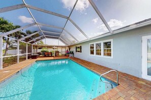 Une piscine entourée de parois en verre, un espace patio et une maison à l’extérieur bleu clair.