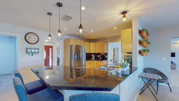 Una cocina moderna con una isla central, iluminación colgante y una zona de comedor con sillas azules.