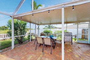 Un patio couvert avec une table et des chaises, un barbecue et une vue sur l’extérieur.