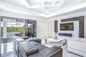 A modern living room with a large sectional sofa, a white armchair, a coffee table, and a TV mounted on the wall. - Dog-friendly pool home with outdoor kitchen, game room, cabana, and pool spa (Cape Coral)