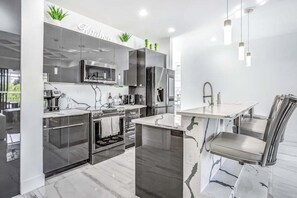 A modern kitchen with stainless steel appliances, a marble island, and a dining area with a chair. - Dog-friendly pool home with outdoor kitchen, game room, cabana, and pool spa (Cape Coral)