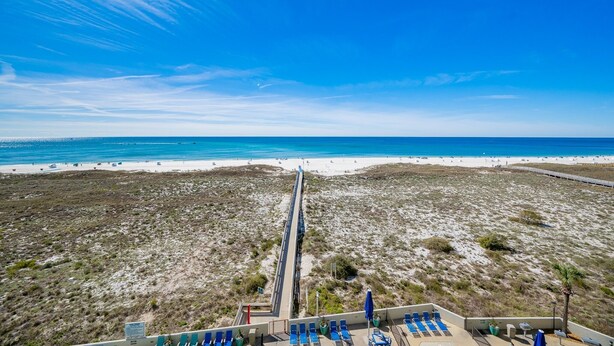 A beach view with a long pier, blue lounge chairs, and a clear sky. - Phoenix Vi 6607 1 Bedroom Condo (Orange Beach)
