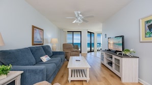 A living room with a sofa, coffee table, TV, and a ceiling fan. - Phoenix Vi 6607 1 Bedroom Condo (Orange Beach)