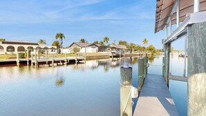 Un hôtel situé au bord de l’eau, doté d’un quai, de palmiers et offrant une vue sur un ciel dégagé.
