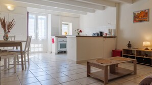 A spacious living area with a dining table, chairs, a kitchen in the background, and a painting on the wall. - Charming One-Bedroom Apartment in the Heart of Vals-les-Bains (Vals-les-Bains)