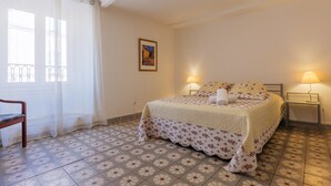 A bedroom with a bed, two bedside lamps, a chair, a window with curtains, and a picture on the wall. - Charming One-Bedroom Apartment in the Heart of Vals-les-Bains (Vals-les-Bains)